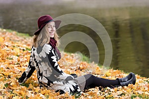 Woman in a floral patterned coat and wine red hat in the park, by the river. Happy girl, colorful autumn forest. Portrait of lady