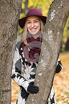 Woman in a floral patterned coat and wine red hat in the park, by the river. Happy girl, colorful autumn forest. Portrait of lady