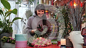 Woman florist creating rose bouquet at flower boutique. Happy flowers seller making gift bouquet from roses in shop