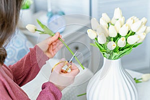 Woman florist cutting stem of tulips flowers with scissors and putting in vase on coffee table. Composing bouque.