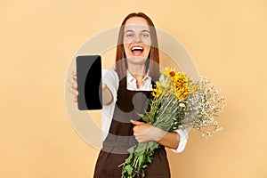 Woman florist showing smartphone with empty display holding beautiful flowers and plants in a flower shop standing isolated over