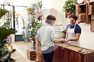 Woman In Florists Shop Making Contactless Payment At Sales Desk Holding Credit Card To Reader