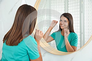 Young woman flossing her teeth in bathroom. Cosmetic dentistry