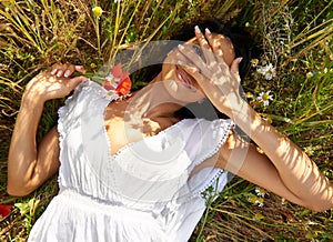 Woman, flowers and lying in field for portrait, peek or smile in spring, vacation or sunshine in nature. Girl, happy and