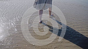 A woman in a flowing dress enters the ocean on a windy sunny day