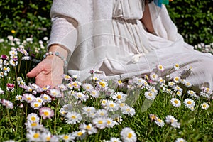 A woman in a flowing white dress gracefully touches a field of daisies, embodying tranquility amidst the vibrant