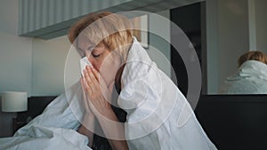 A woman with a flu, feeling bad, blowing into her nose, wrapped in a white blanket. Doctor`s medical help