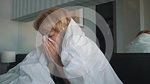 A woman with a flu, feeling bad, blowing into her nose, wrapped in a white blanket. Doctor`s medical help