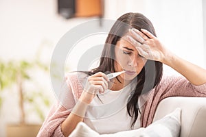 Woman with flu having fever measures temperature by holding thermometer in her mouth