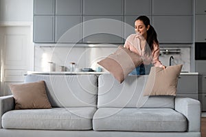 Woman fluffing cushions on a sofa in a neat, stylish room