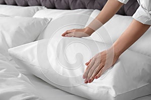 Woman fluffing soft pillow in bedroom