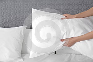 Woman fluffing soft pillow in bedroom, closeup