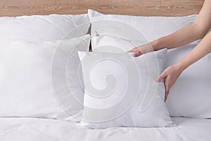 Woman fluffing soft pillows on bed