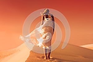 Woman in fluttering dress. Desert and sand dunes. Red sky.