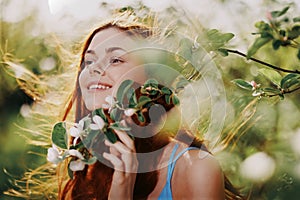 A woman with flying hair in spring stands near a blooming apple tree and smiles with teeth, laughing looks into the