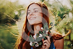 A woman with flying hair in spring stands near a blooming apple tree and smiles with teeth, laughing looks into the