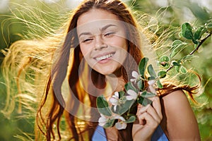 A woman with flying hair in spring stands near a blooming apple tree and smiles with teeth, laughing looks into the