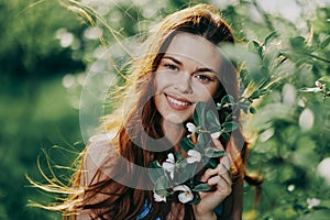 A woman with flying hair in spring stands near a blooming apple tree and smiles with teeth, laughing looks into the