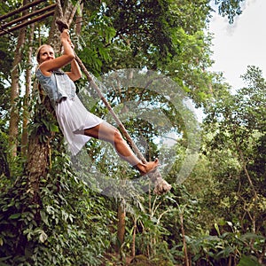 Woman flying high on rope swing on wild jungle background