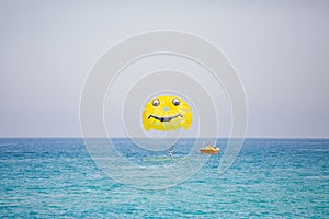 Woman flying on a yellow parachute with smiling face on it
