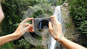 Woman focuses on the phone screen and takes a photo of the waterfall close-up