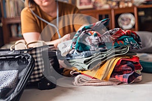 A woman folds clothes from a pile of selected belongings and puts them in luggage on the bed. Packing to go on a getaway vacation