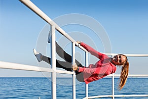 Woman fool around sitting on handrail near sea