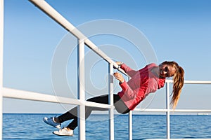 Woman fool around sitting on handrail near sea