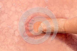 Woman foot in salt flakes in pink water, spa