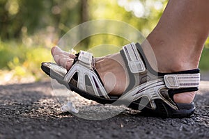 Woman foot in sandals steps on a lost wireless headphones that lies on a asphalt sidewalk, outdoors, against a blurred