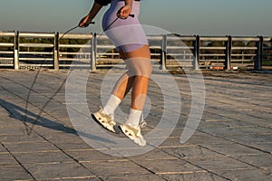 A woman with footwear and shorts jumps rope on concrete