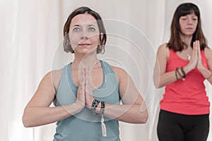 The woman in the foreground with the hands in Namaste`s gesture. Close up of girl meditating at yoga studio in group.