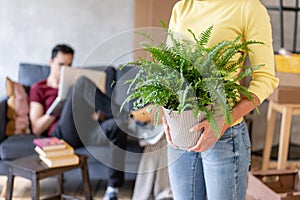 Woman in the foreground holding a fern flower in her hands. Young couple moving to a new apartment together. Relocation