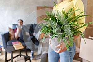 Woman in the foreground holding a fern flower in her hands. Young couple moving to a new apartment together. Relocation