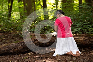 Woman in Forest Preserve with Bible Kneeling in Prayer