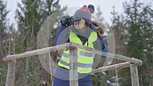 Woman forester on tower looking through binoculars in forest