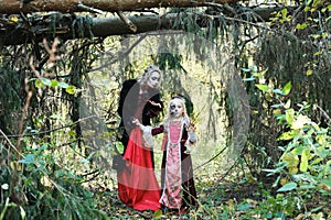 A woman in the form of a vampire or a sorceress poses in the forest with a girl in fairy-tale makeup and medieval dress