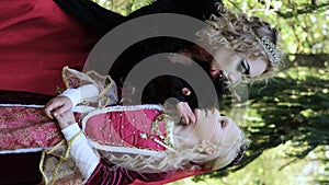 A woman in the form of a vampire or a sorceress poses in the forest with a girl in fairy-tale makeup and medieval dress