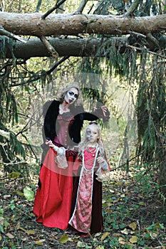 A woman in the form of a vampire or a sorceress poses in the forest with a girl in makeup and a medieval dress