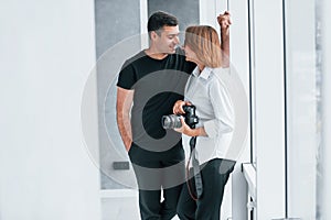 Woman in formal clothes and with camera in hand standing inside of empty room with man
