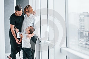 Woman in formal clothes and with camera in hand standing inside of empty room with man and little boy