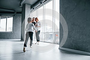 Woman in formal clothes and with camera in hand standing inside of empty room with man and little boy that running and having fun