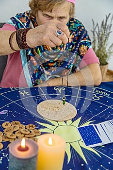 Woman fortune teller fortune telling pendulum. Selective focus.