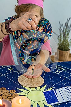 Woman fortune teller fortune telling pendulum. Selective focus.