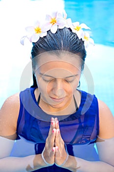 Woman with frangipani flowers in her hair, praying pose in swimming pool