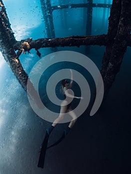 Woman free diver swims underwater on deep in transparent ocean. Freediving under the pier