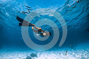 Woman freediver glides underwater with fins over sandy bottom