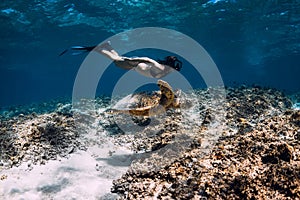 Woman freediver glides underwater with sea turtle.