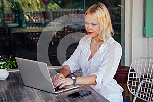 Woman freelance freelancer with laptop on the beach sitting in summer cafe .business lady remote work surfer surfing