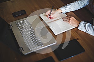 Woman freelancer female hands with pen writing on notebook at home or office.